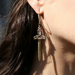 Close-up of a person wearing a unique earring with a dagger design and red gemstones.