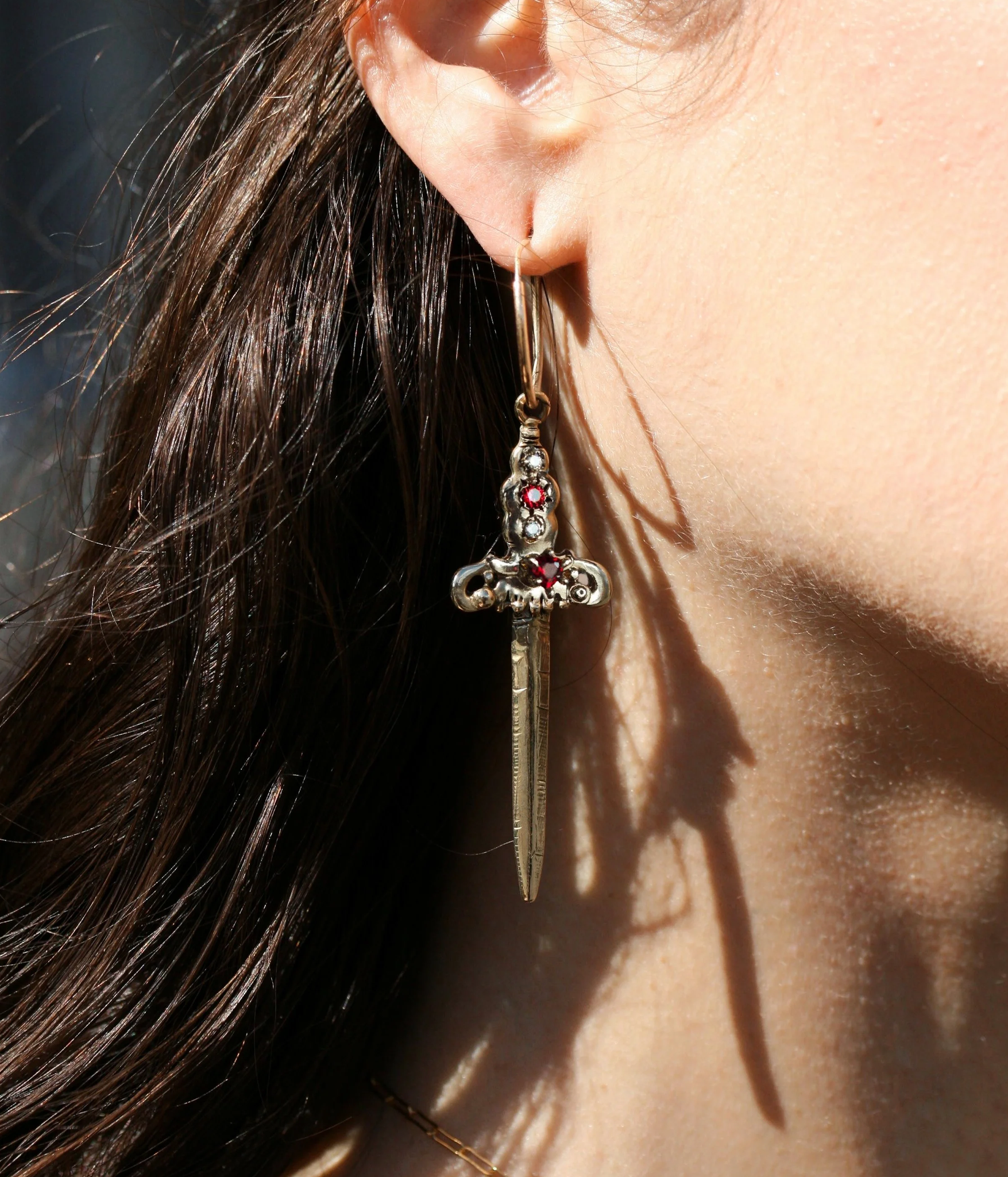 Close-up of a person wearing a unique earring with a dagger design and red gemstones.