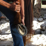 Person holding a horse's hoof with a metal shoe, outdoors on a rocky ground.
