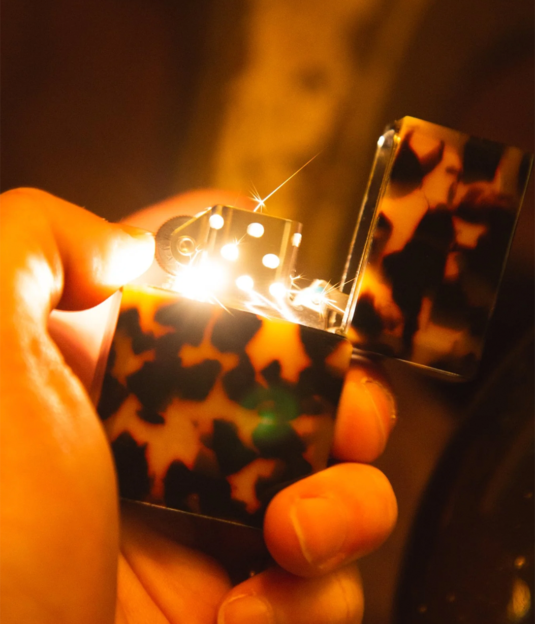 Hand holding a zippo lighter with a colorful case, blurred background