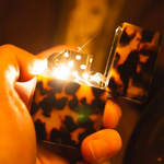 Hand holding a zippo lighter with a colorful case, blurred background