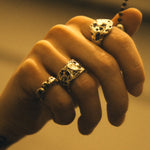 Hand wearing two silver rings with intricate designs on a neutral background