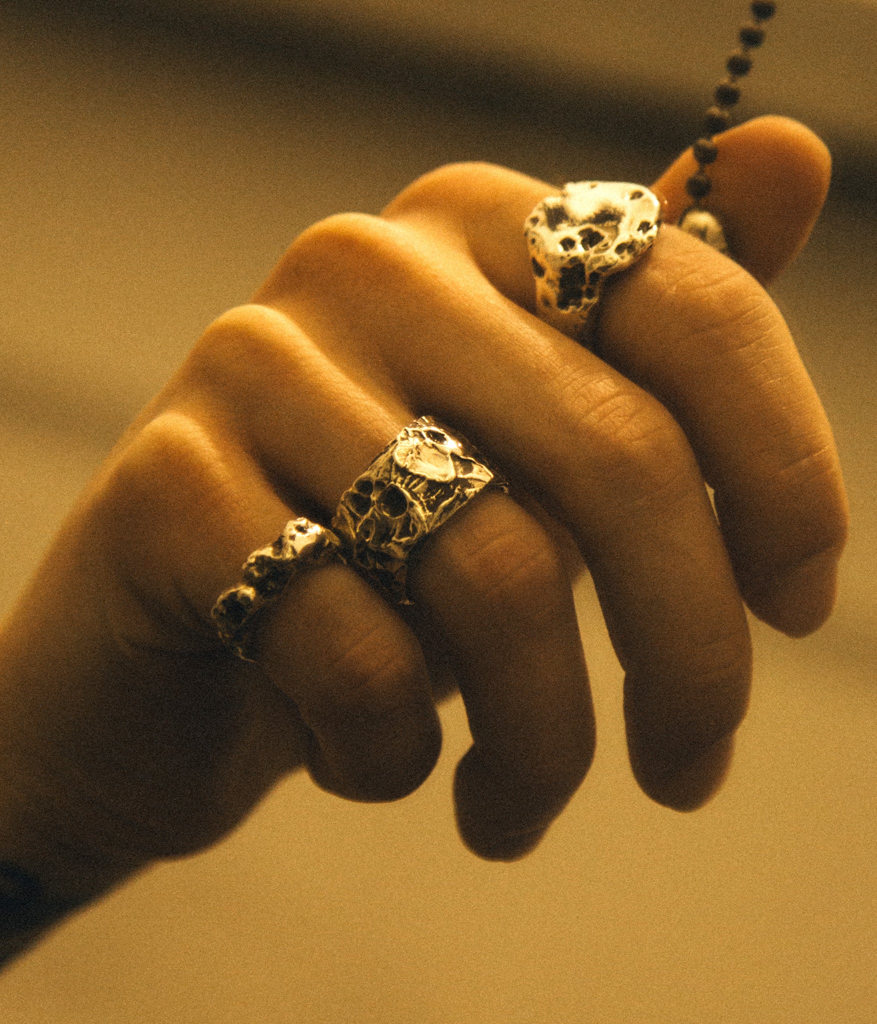 Hand wearing two silver rings with intricate designs on a neutral background