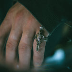 Hand wearing a detailed ring with a heart design against a blurred background