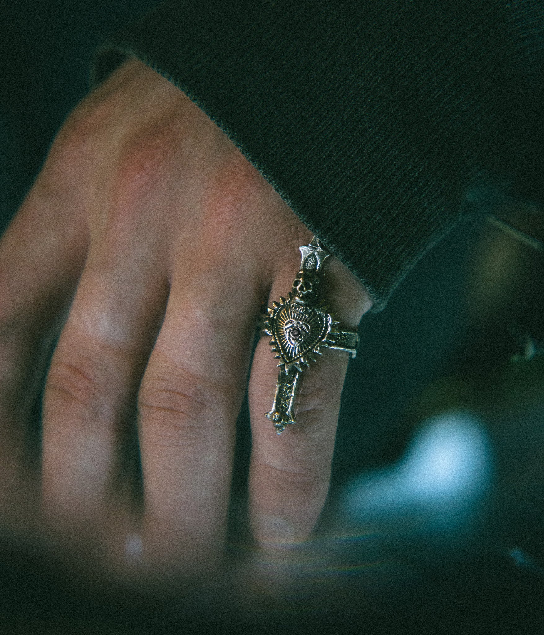 Hand wearing a detailed ring with a heart design against a blurred background