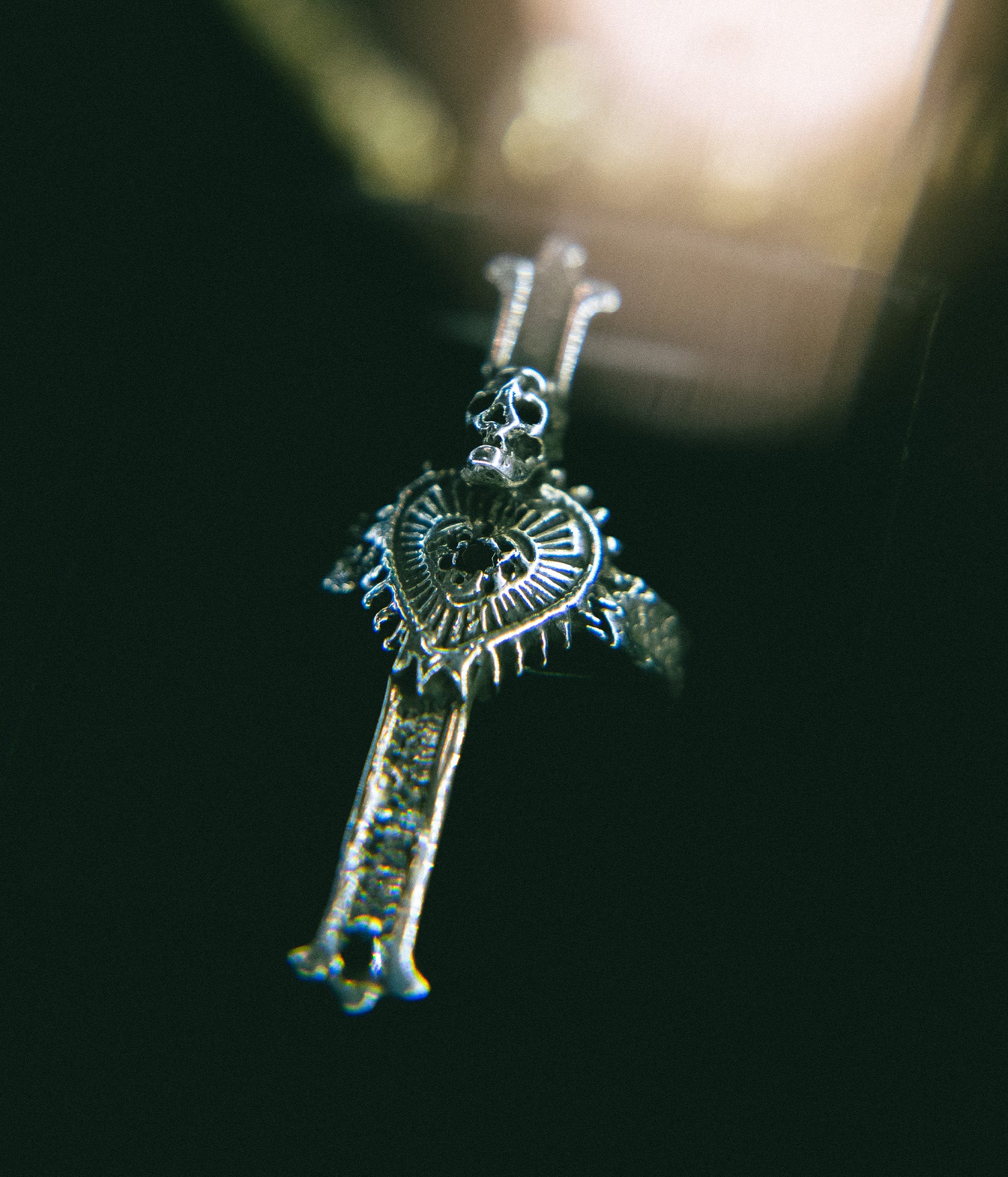 Silver key-shaped pendant with intricate design on a dark background