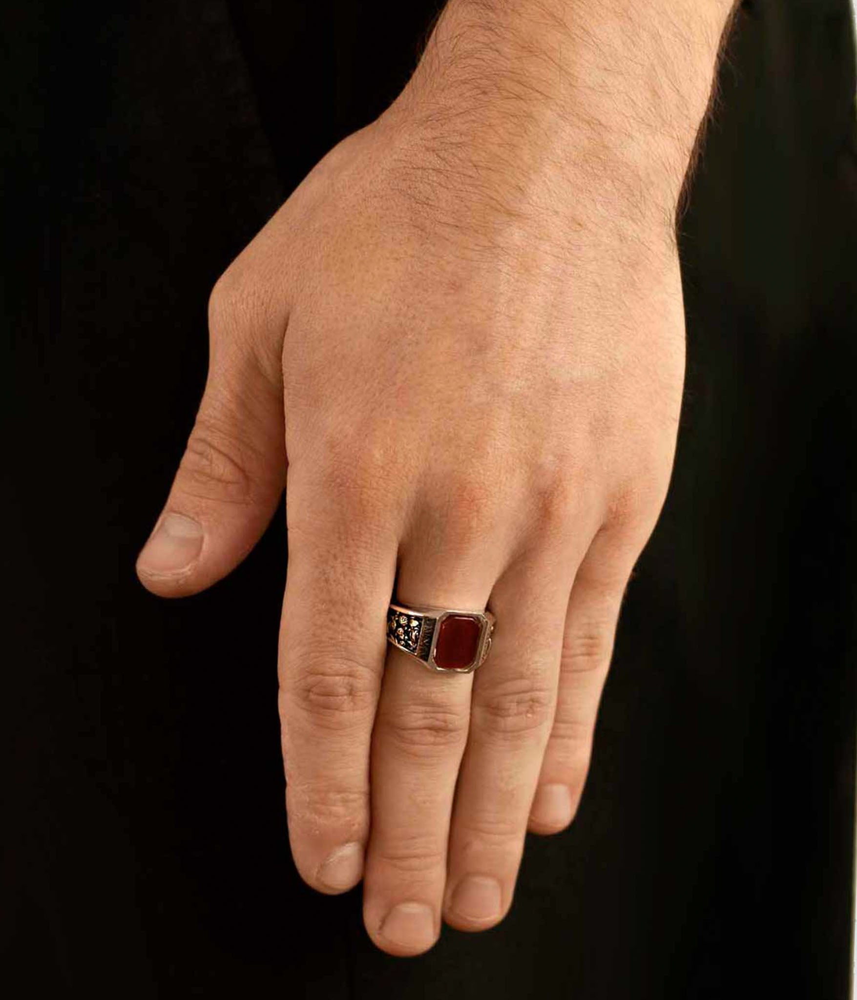 Hand wearing a ring with a red stone on a black background