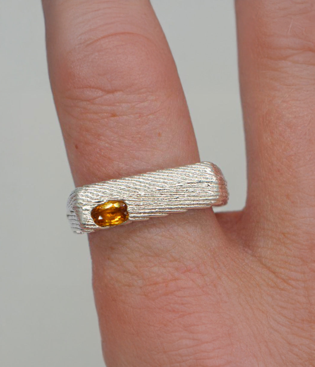 Silver ring with a yellow gemstone on a finger against a neutral background