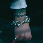 Silver bracelet on a wrist with a tattoo, against a dark background