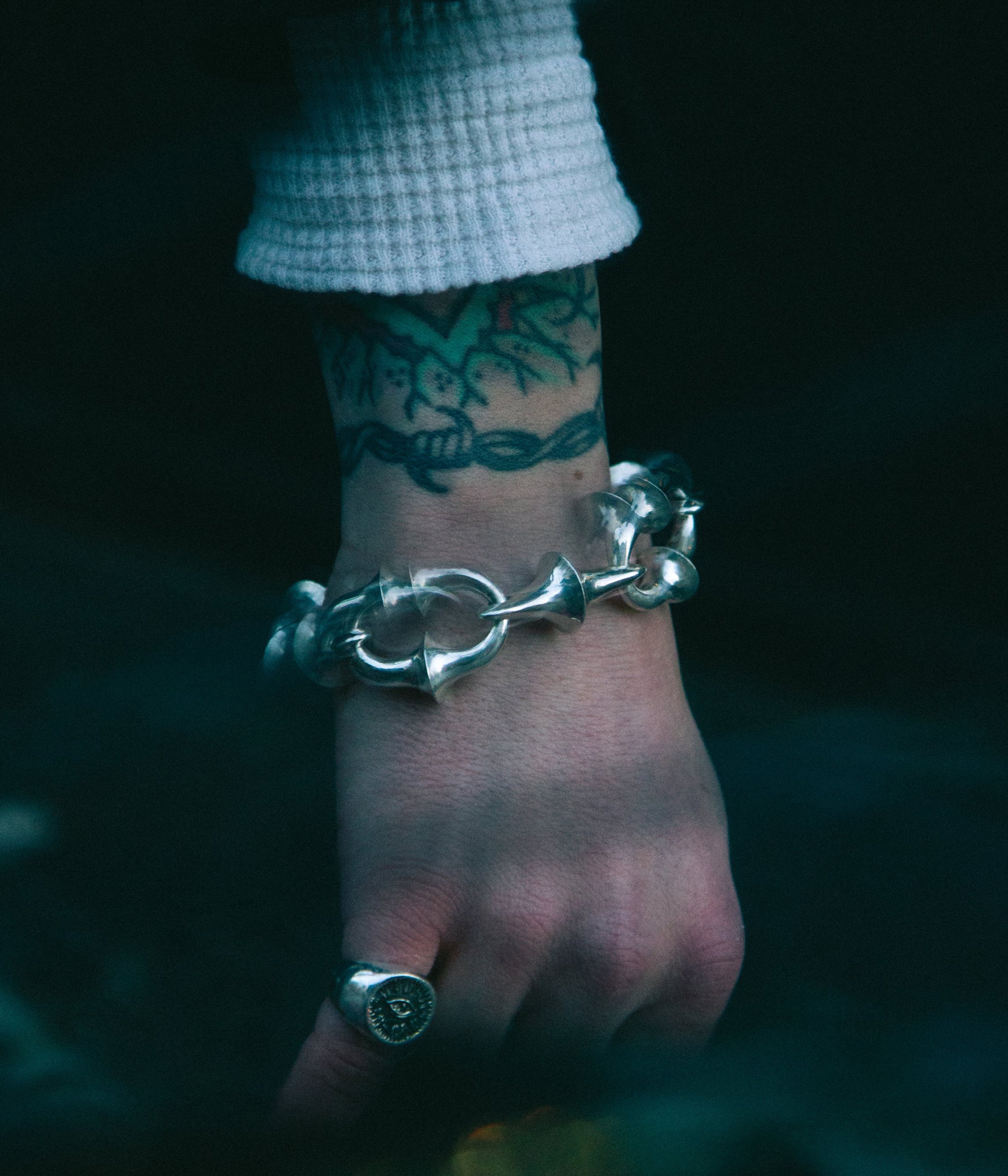 Silver bracelet on a wrist with a tattoo, against a dark background