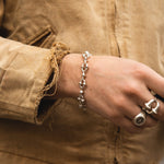 Hand wearing a silver bracelet and ring on a beige jacket background