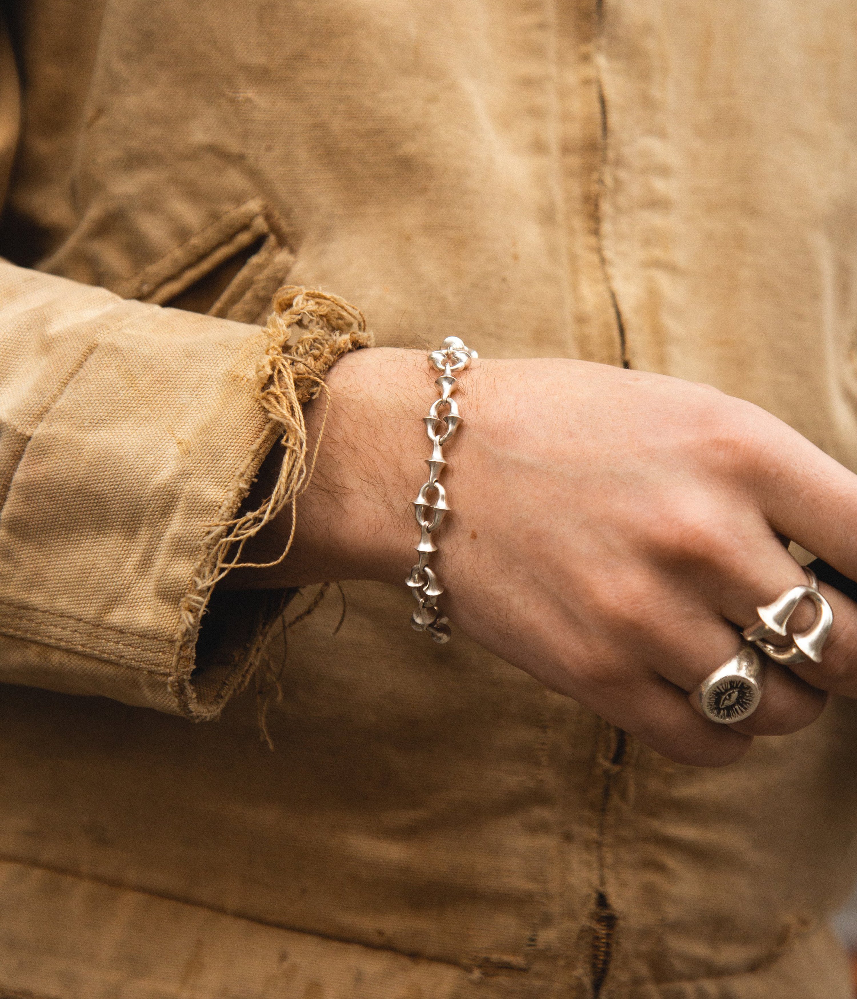 Hand wearing a silver bracelet and ring on a beige jacket background