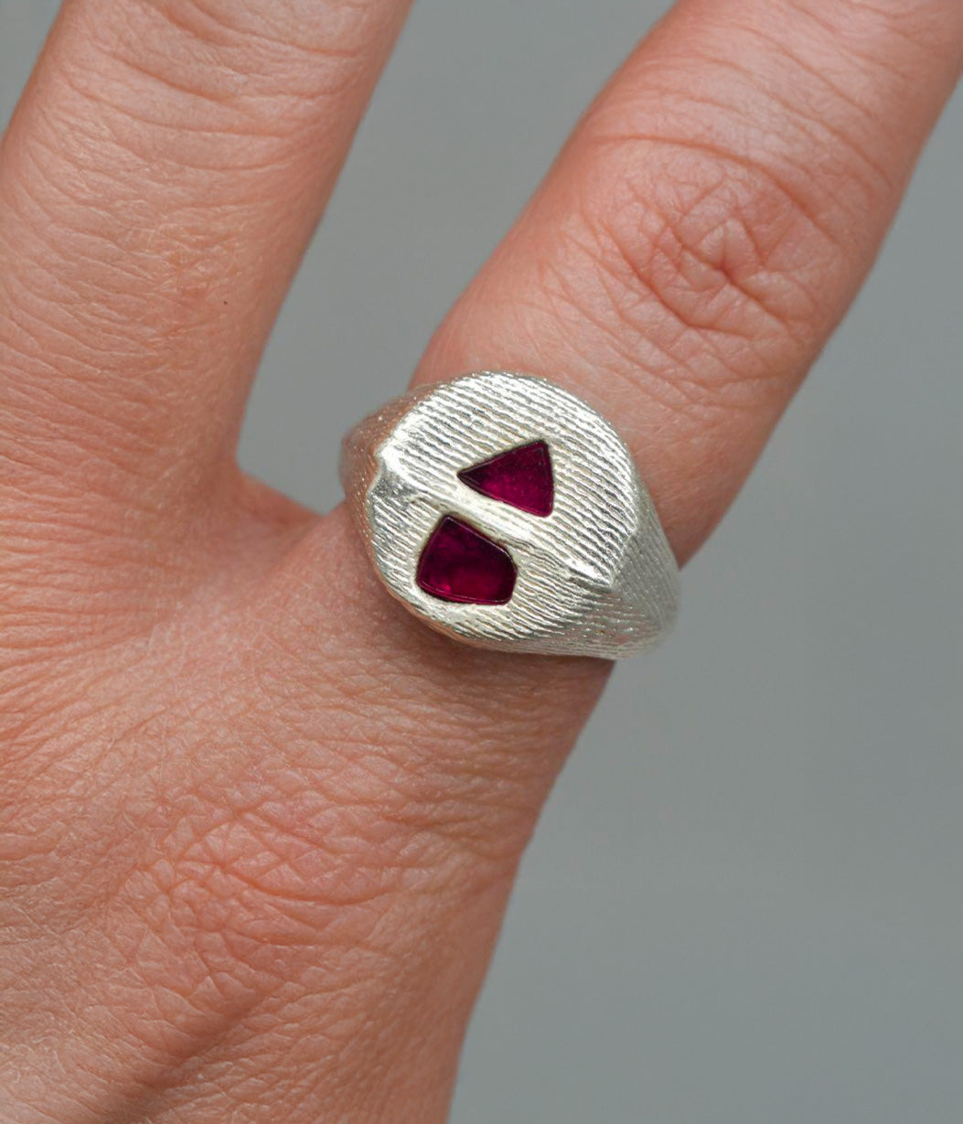 Silver ring with red gemstones on a finger against a gray background