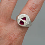 Silver ring with red gemstones on a finger against a gray background