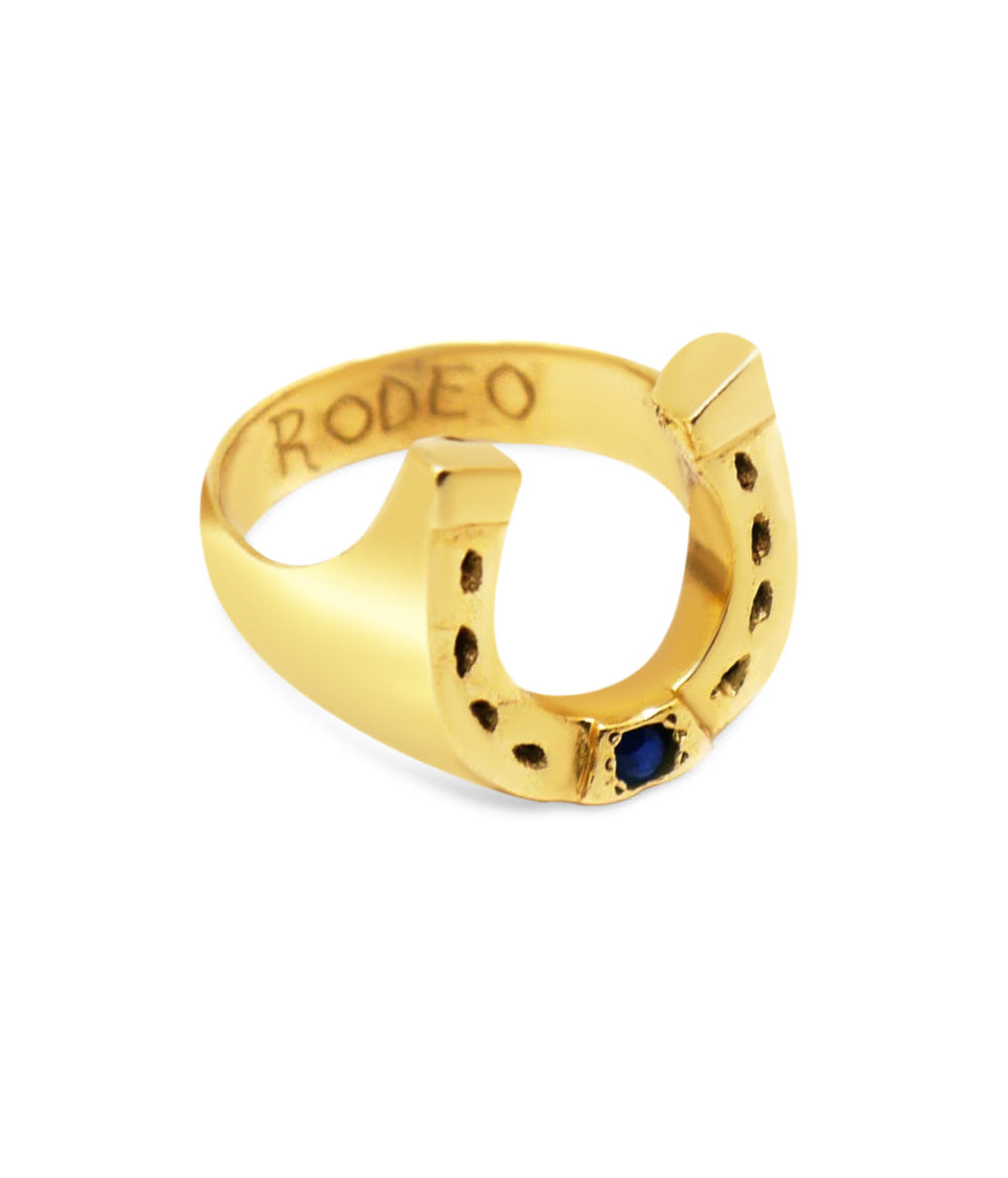 Gold ring with 'RODEO' engraving and blue gemstone on a white background