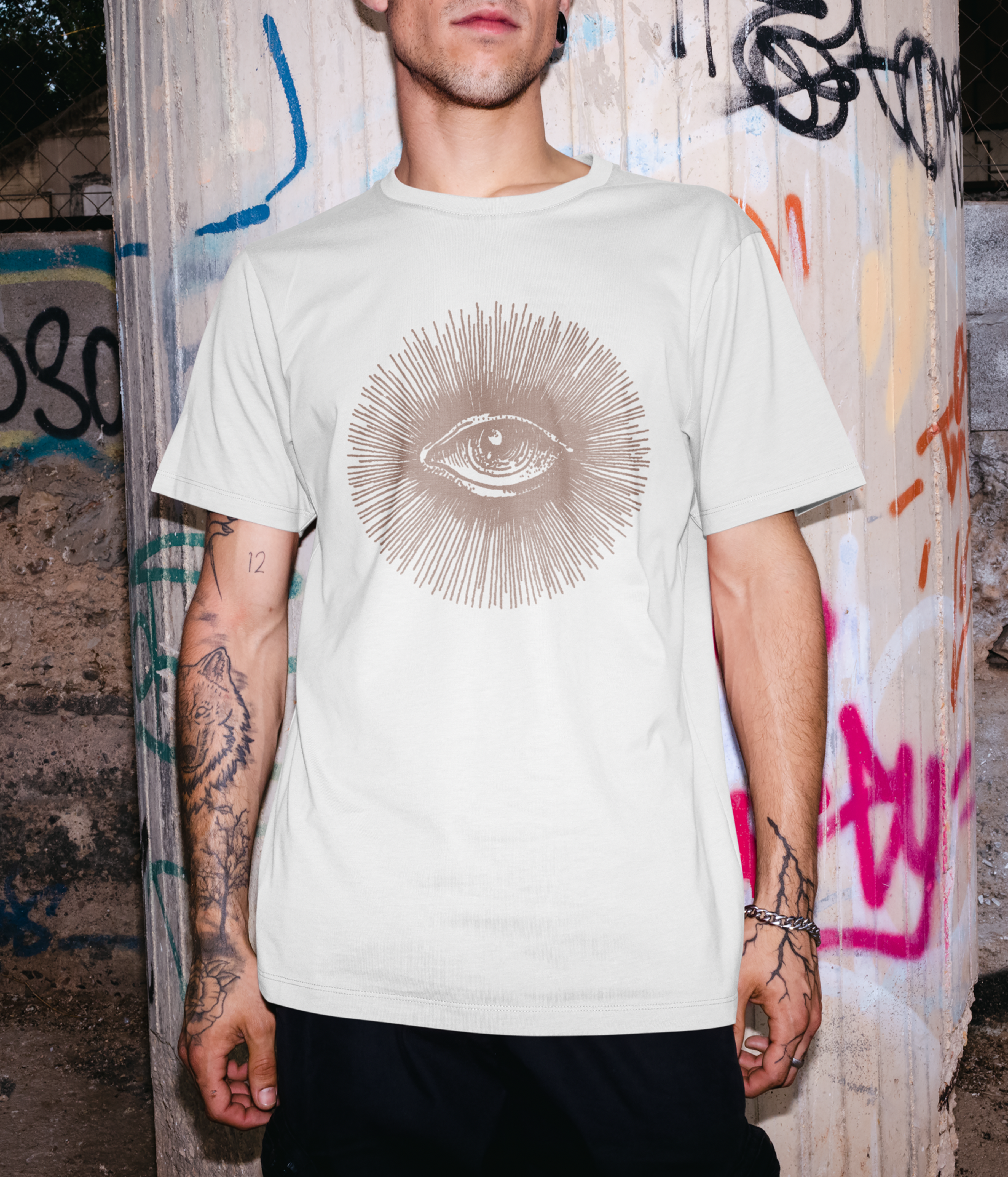 Person wearing a white t-shirt with a graphic design in front of a graffiti-covered wall.