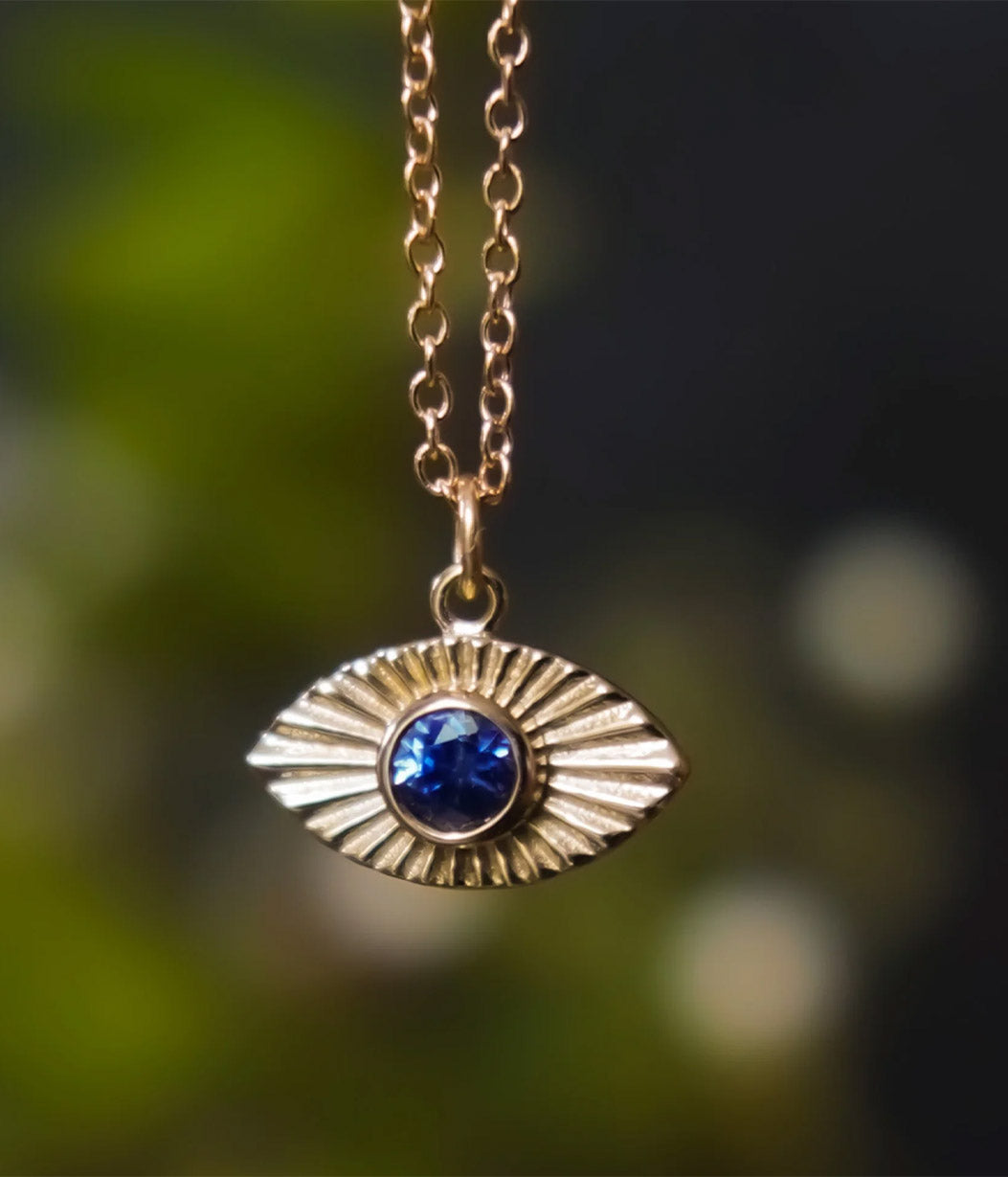 Gold necklace with an eye-shaped pendant featuring a blue gemstone against a blurred green background