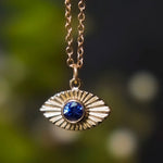 Gold necklace with an eye-shaped pendant featuring a blue gemstone against a blurred green background
