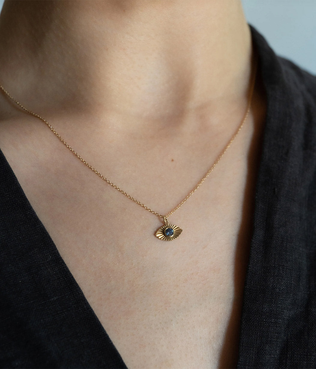 Gold necklace with a pendant on a person wearing a black top.