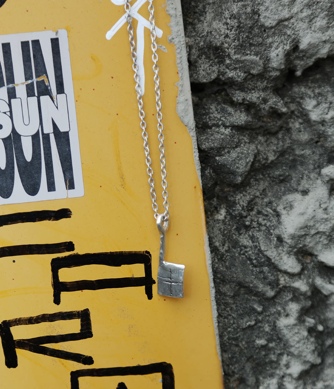 Silver necklace with a square pendant on a yellow background with black text