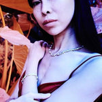 Person with dark hair and makeup, wearing a red top and necklace, holding an orange umbrella.