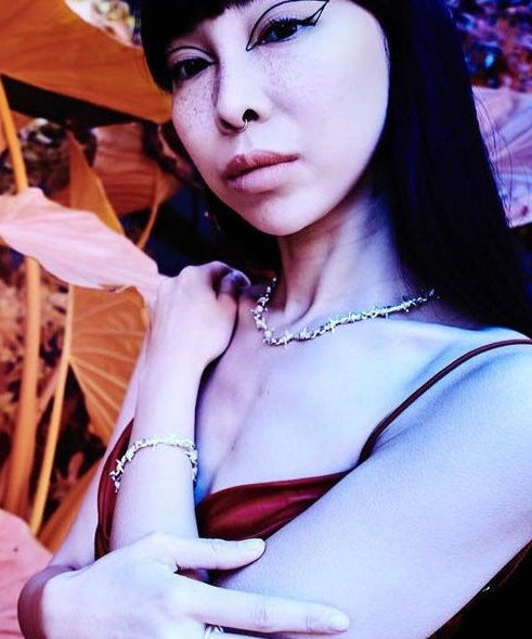 Person with dark hair and makeup, wearing a red top and necklace, holding an orange umbrella.