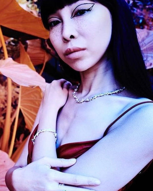 Person with dark hair and makeup, wearing a red top and necklace, holding an orange umbrella.