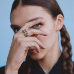 Close-up of a person with braided hair wearing a colorful ring on a light blue background