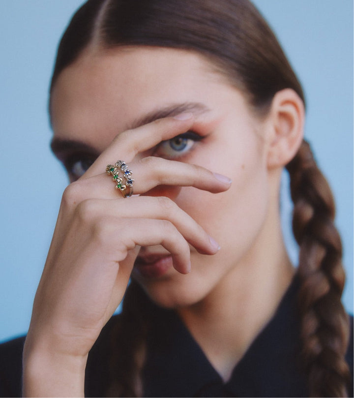 Close-up of a person with braided hair wearing a colorful ring on a light blue background