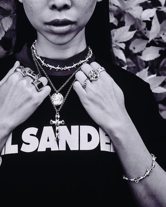 Person wearing multiple necklaces and rings with a black shirt 