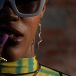 Person wearing large sunglasses and a yellow and green patterned top with a blurred background