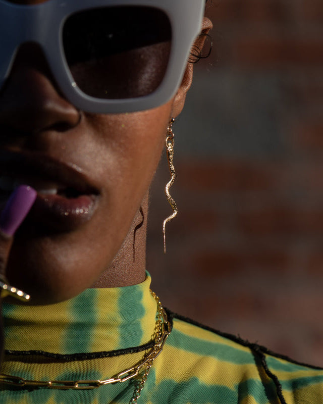 Person wearing large sunglasses and a yellow and green patterned top with a blurred background