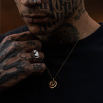 Man with tattoos wearing a necklace with a gold pendant.