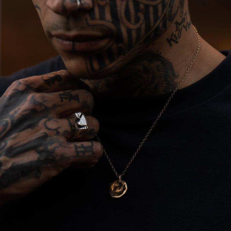Man with tattoos wearing a necklace with a gold pendant.