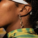 Close-up of a person wearing gold chain earrings with a blurred background