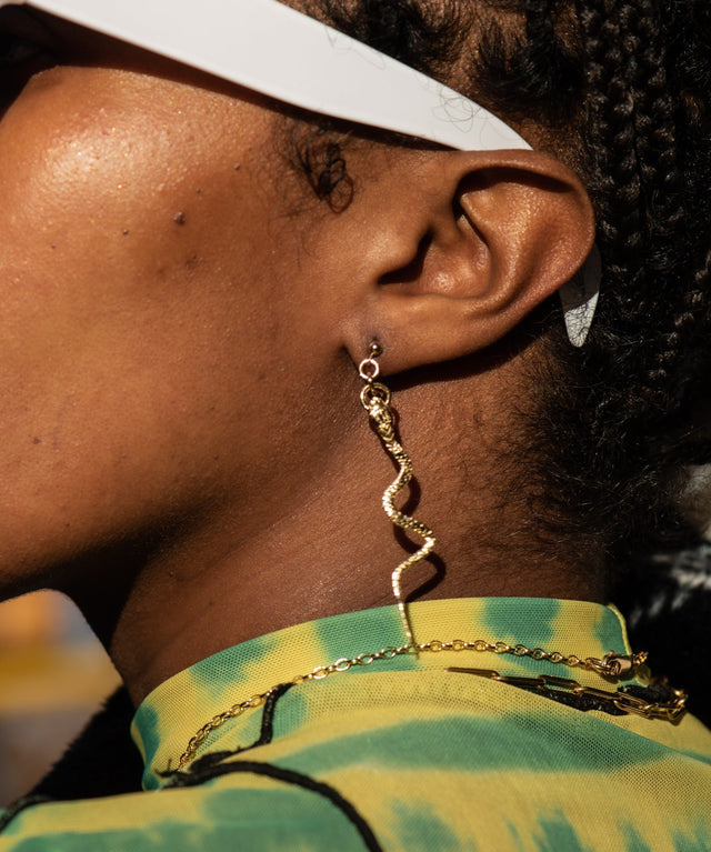 Close-up of a person wearing gold chain earrings with a blurred background