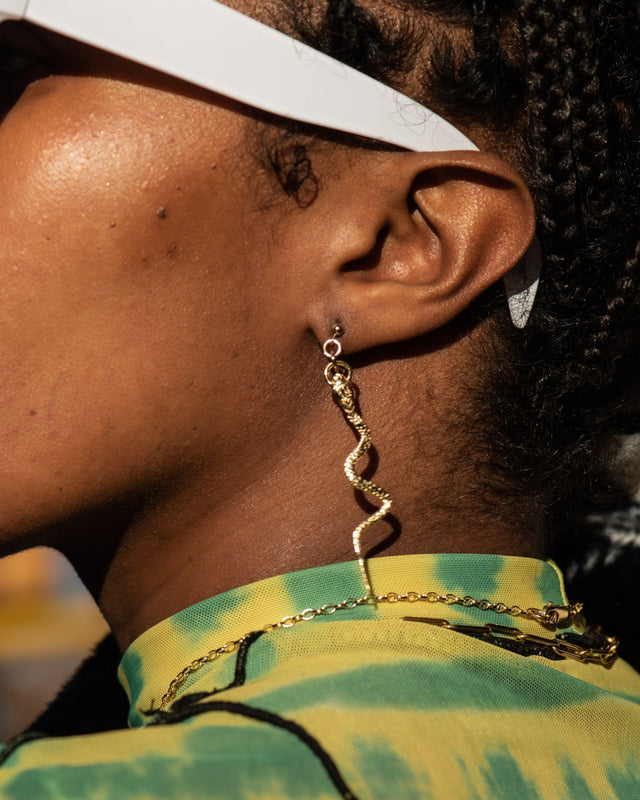 Close-up of a person wearing gold chain earrings with a blurred background
