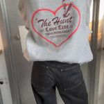 Person wearing a gray hoodie with a red heart design and text.