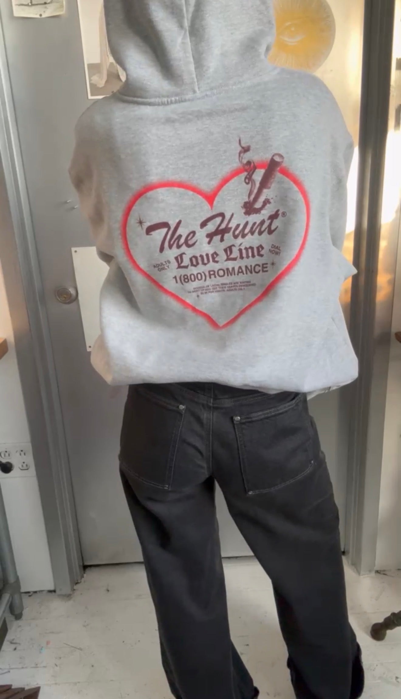 Person wearing a gray hoodie with a red heart design and text.