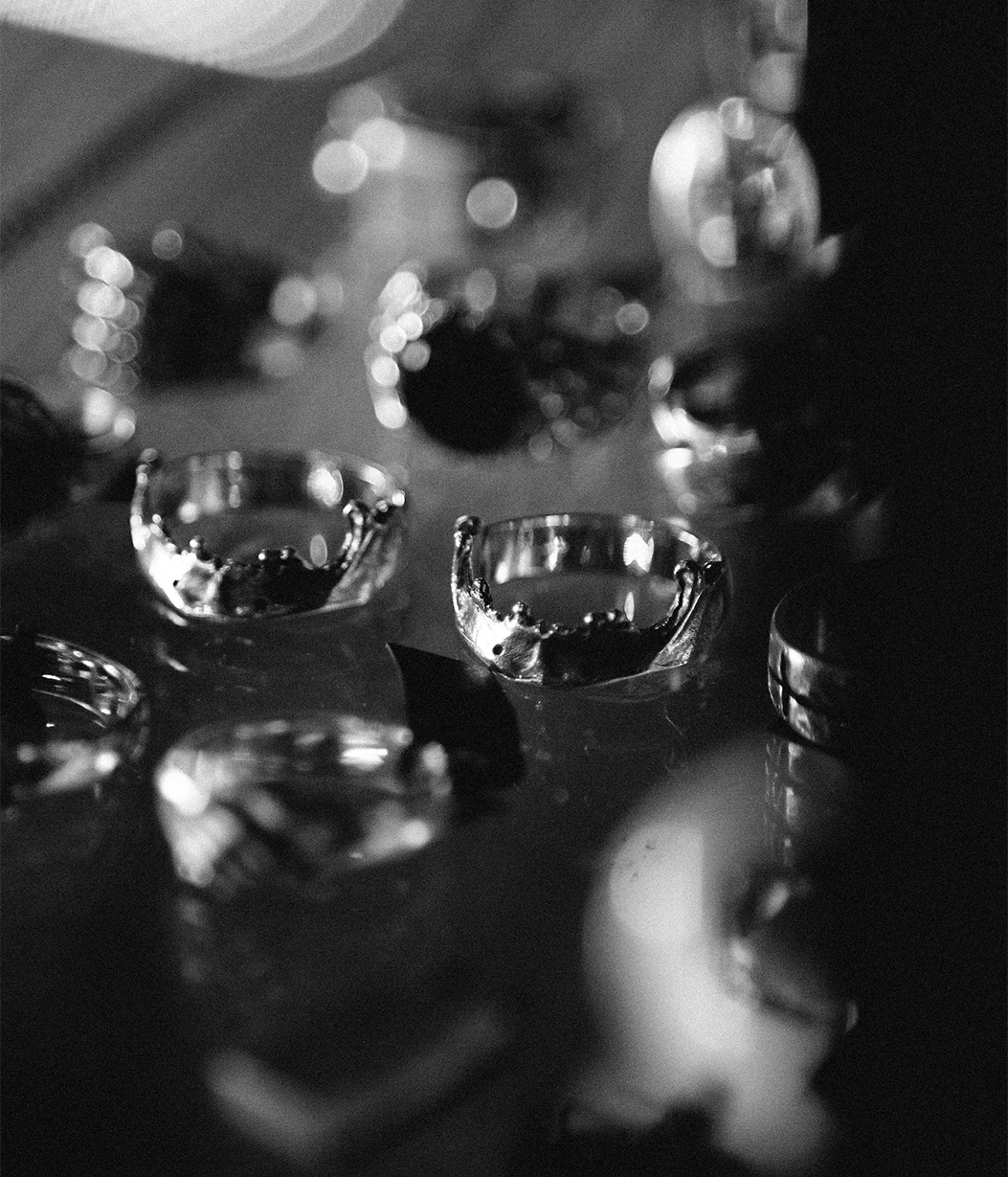 A close-up black and white photograph of several clear glass rings displayed on a reflective surface, with shallow depth of field and blurred reflections in the background.