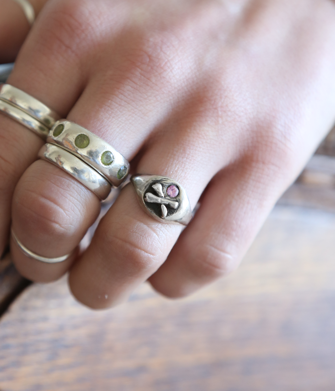 Close-up of a hand wearing two silver rings with heart designs on a wooden surface.