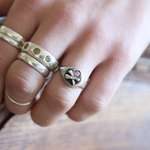 Close-up of a hand wearing two silver rings with heart designs on a wooden surface.