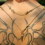Gold necklace with star and arrow pendants on a person with tattoos