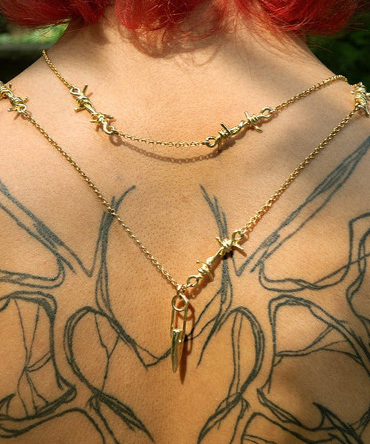 Gold necklace with star and arrow pendants on a person with tattoos