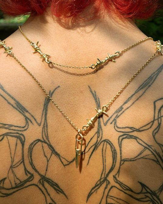 Gold necklace with star and arrow pendants on a person with tattoos