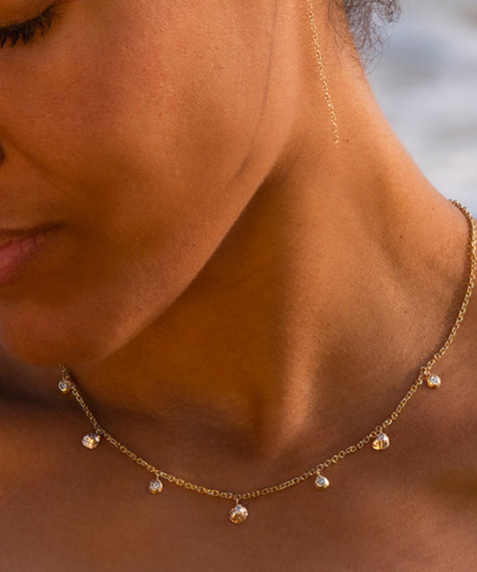 Woman wearing a gold necklace with a blurred beach background