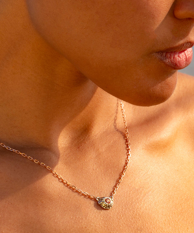 Close-up of a person wearing a delicate necklace with a small pendant against a blurred natural background.