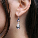 Close-up of a silver teardrop earring on an ear with dark hair.