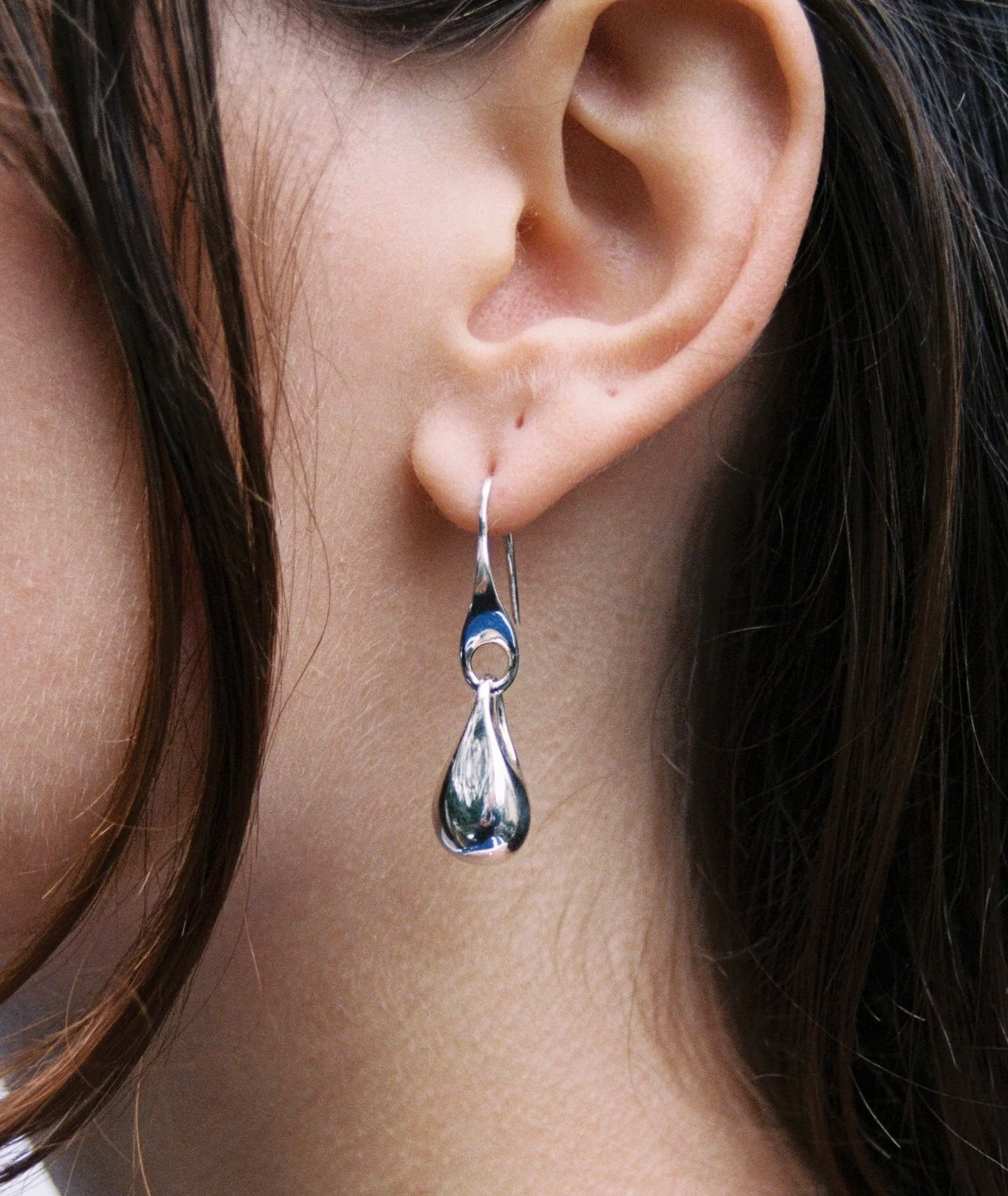 Close-up of a silver teardrop earring on an ear with dark hair.