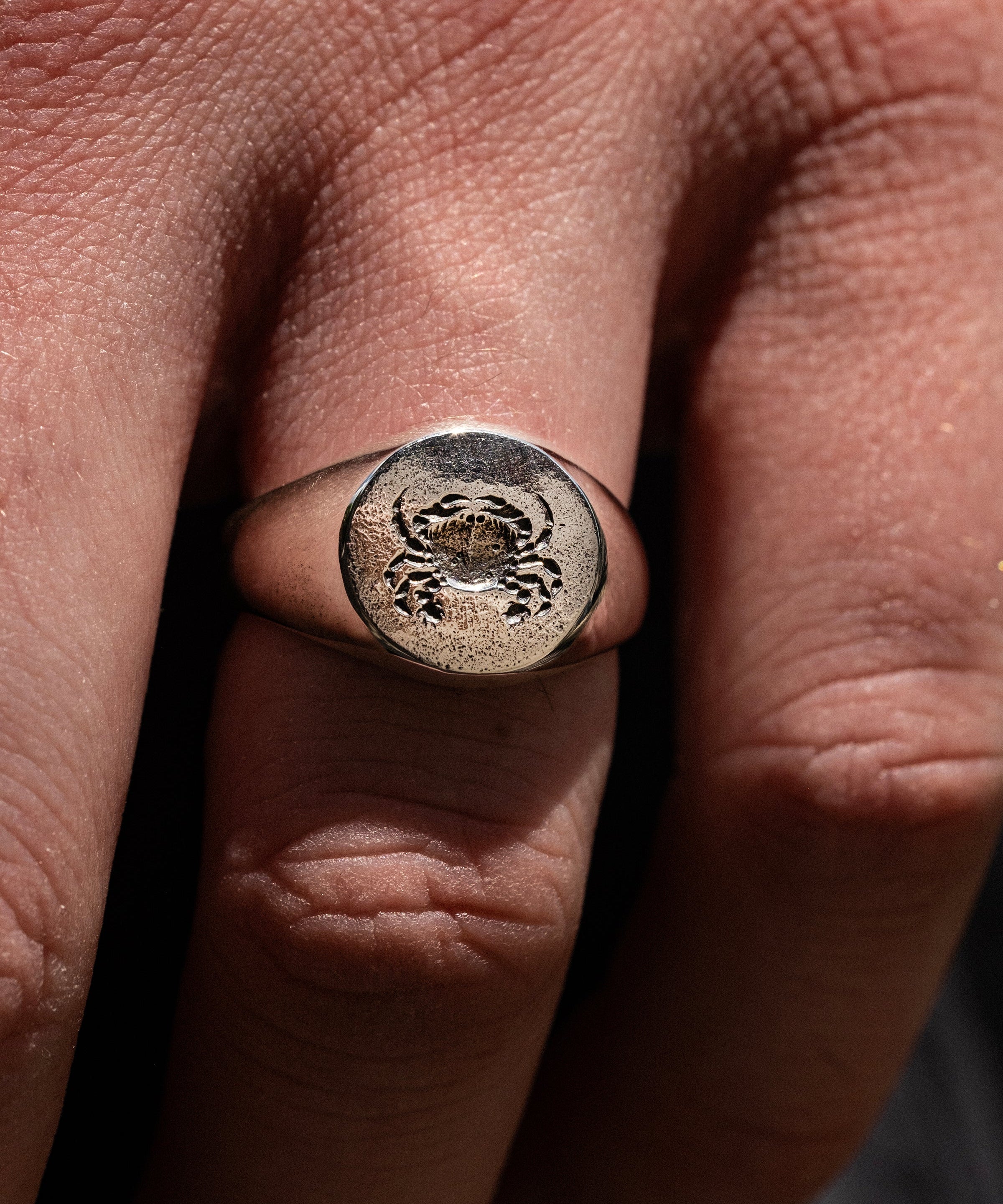Close-up of a hand wearing a silver ring with a design on a finger.